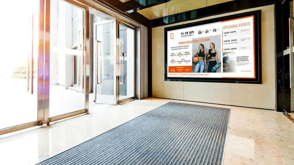 digital signage screen from Reach Media Network featured in gym lobby, displaying fitness class schedule, upcoming events, and sports headlines.